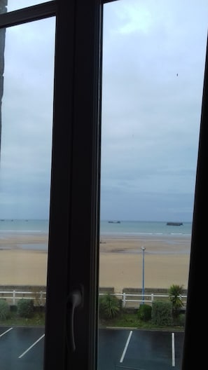 A view of a beach from inside a building, with a parking lot in the foreground. - Le Manoir des Tourelles (Asnelles)