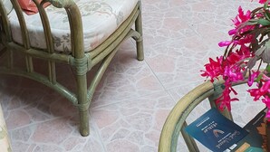 Una habitación con una silla de mimbre, una mesita con un libro, un espejo y una puerta.