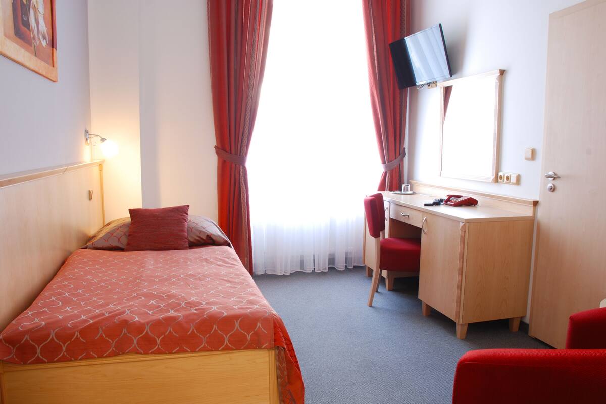 Habitación de hotel con cama, escritorio, silla, televisión y ventana con cortinas.