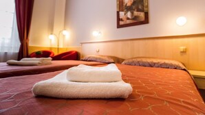 Een hotelkamer met twee bedden, elk met een keurig opgevouwen handdoek. Er zijn wandlampen en een schilderij aan de muur.