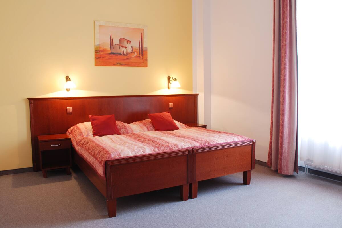 Una cama bien hecha con ropa de cama roja, un cabecero de madera y dos mesitas de noche con lámparas.