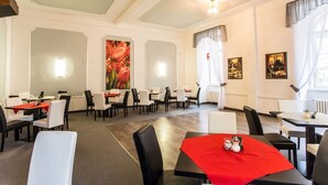 Een eethoek met meerdere tafels en stoelen, een groot schilderij van rode bloemen aan de muur en een plafond met inbouwverlichting.