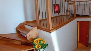 Uma escada de madeira com corrimão de metal, um vaso de girassóis e uma porta vermelha na base.