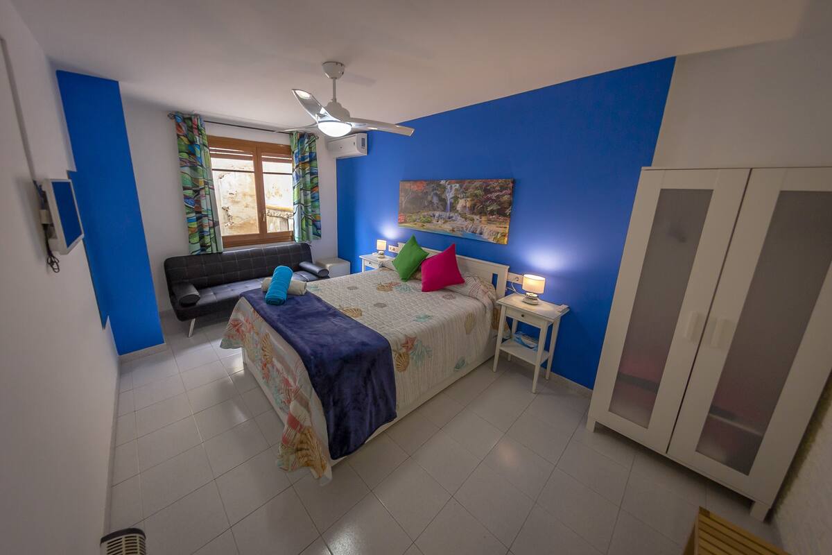 Ein Schlafzimmer mit Bett, Nachttisch, Kleiderschrank, Deckenventilator und einem Fenster mit Vorhängen.