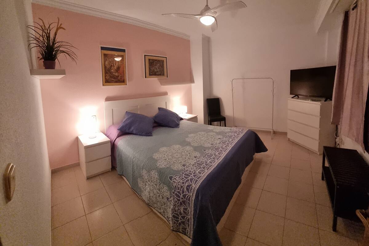 Ein Schlafzimmer mit einem Bett, Nachttischen, einem Deckenventilator, einem Fernseher und einem Kleiderschrank.