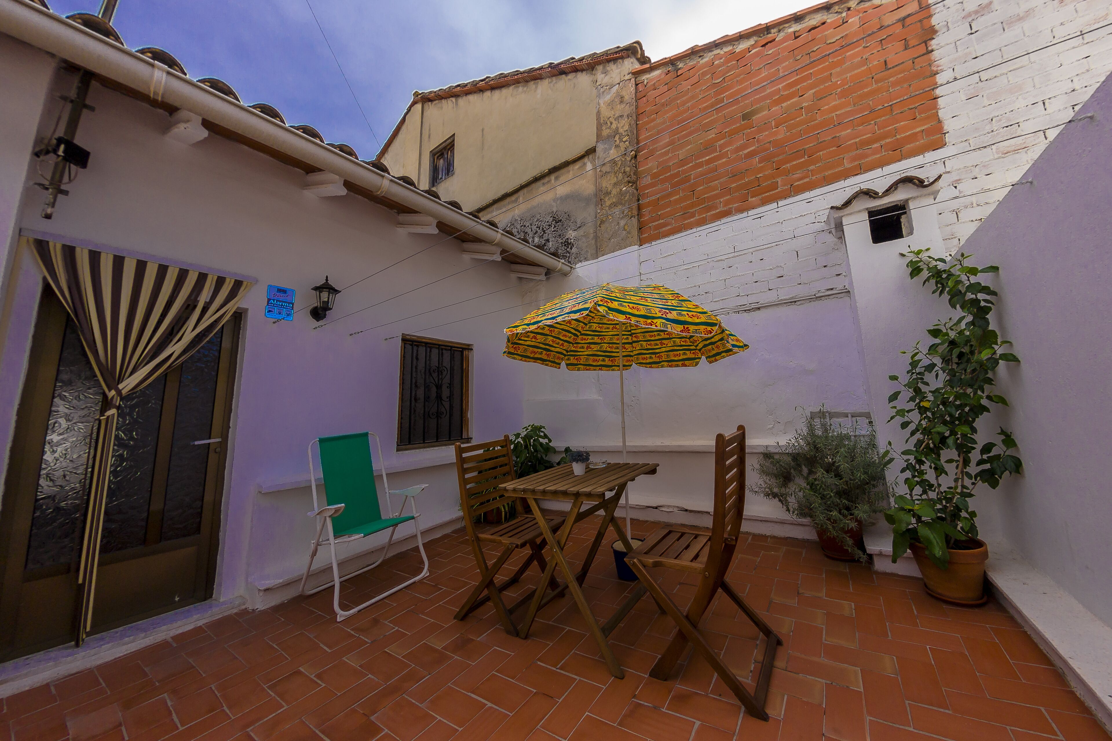 A patio area with a table and chairs, a striped umbrella, and potted plants.