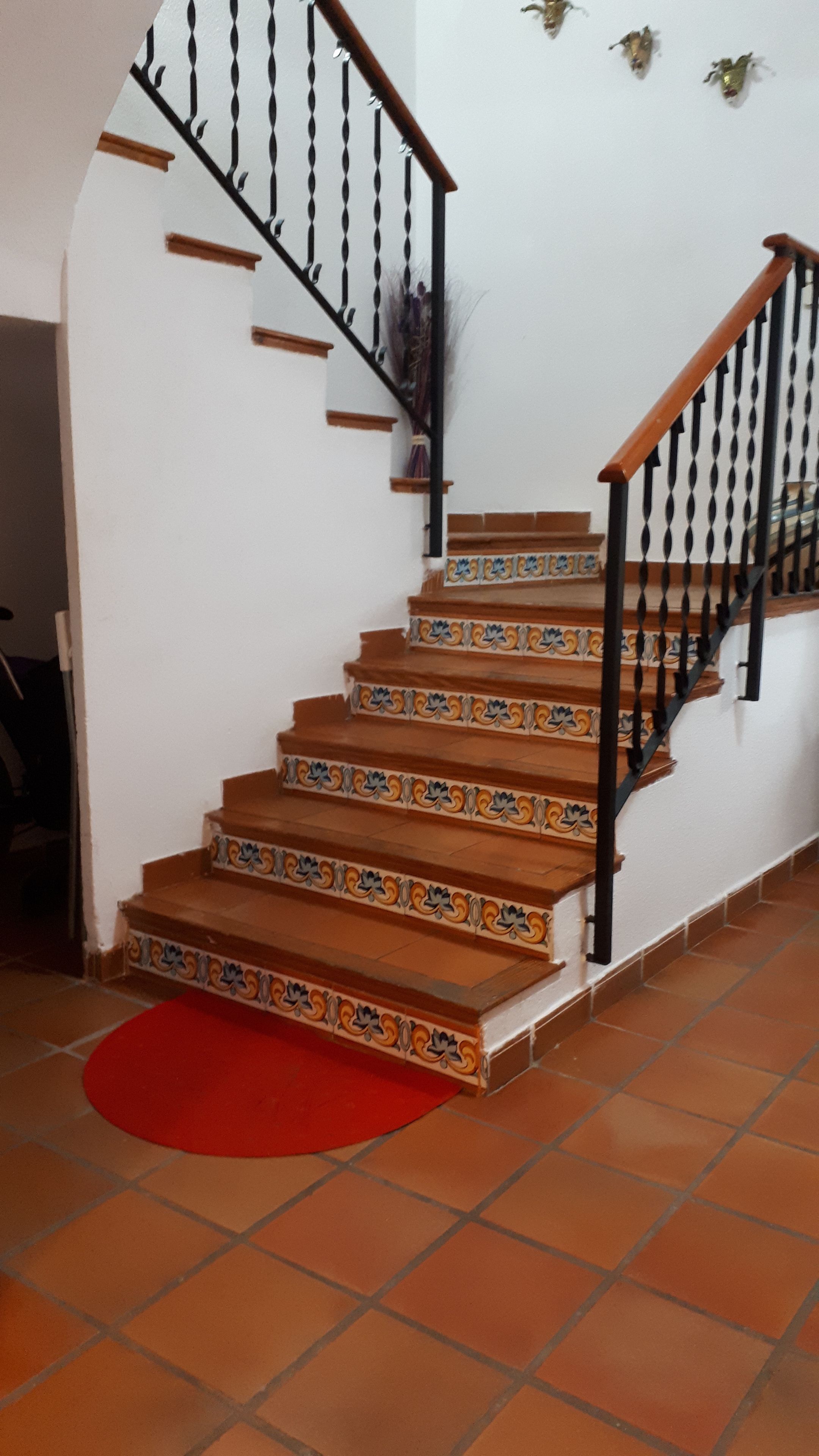 Una escalera con barandilla negra y un tapete rojo al pie.