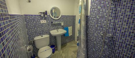 Baño con inodoro, lavabo y zona de ducha, con mosaicos azules y una alfombra de baño azul.