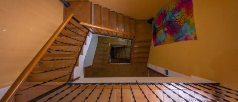 Una escalera con barandilla, suelo de baldosas y un cuadro de colores en la pared.