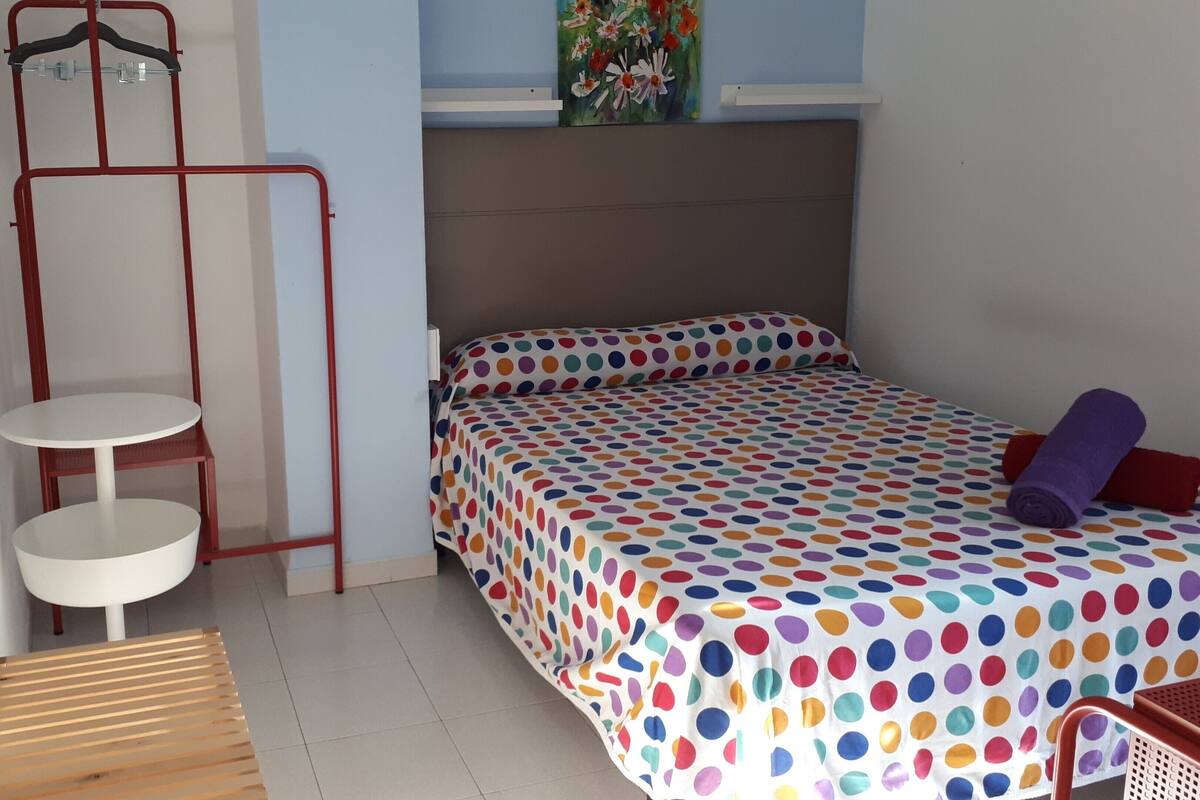 Ein kleiner, ordentlicher Raum mit einem Bett, einem Tischchen und einem Stuhl.