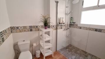 Une salle de bain comprenant des toilettes, une douche, une étagère avec des articles de toilette et une plante en pot.
