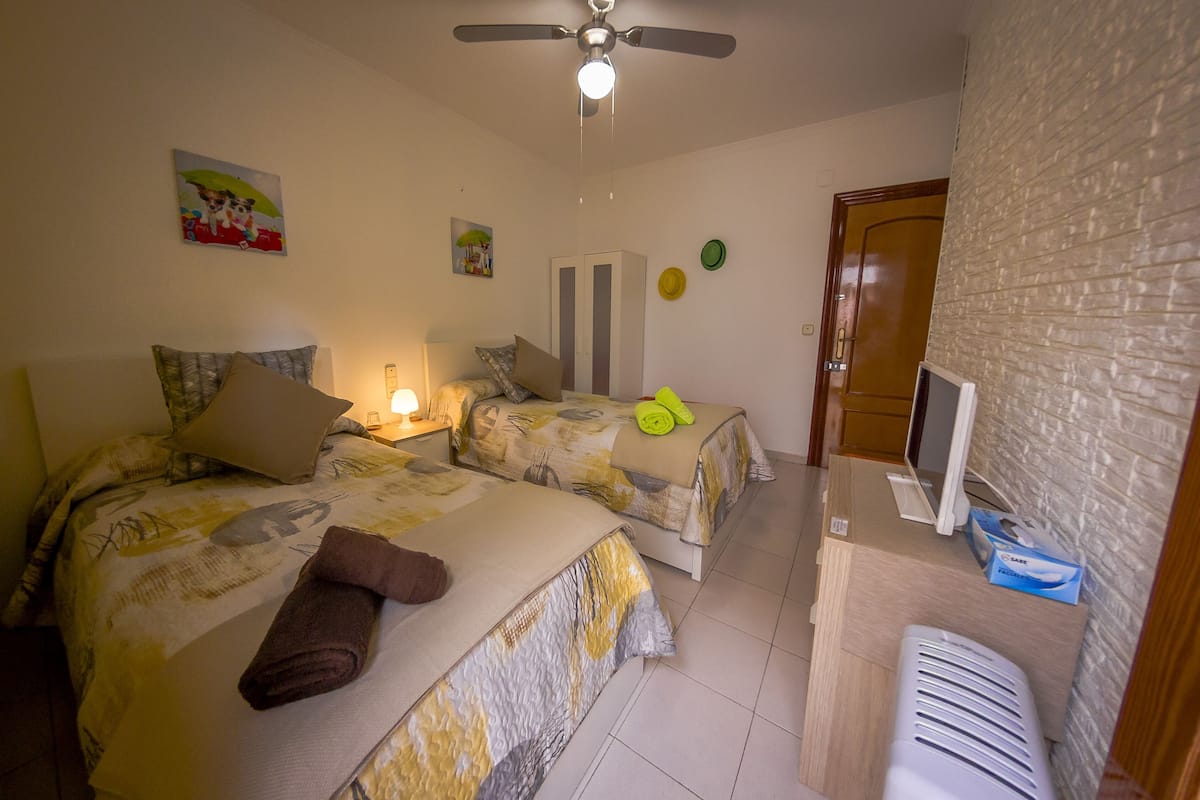 Ein Schlafzimmer mit zwei Betten, einem Deckenventilator, einem Fernseher und einer Ziegelwand.