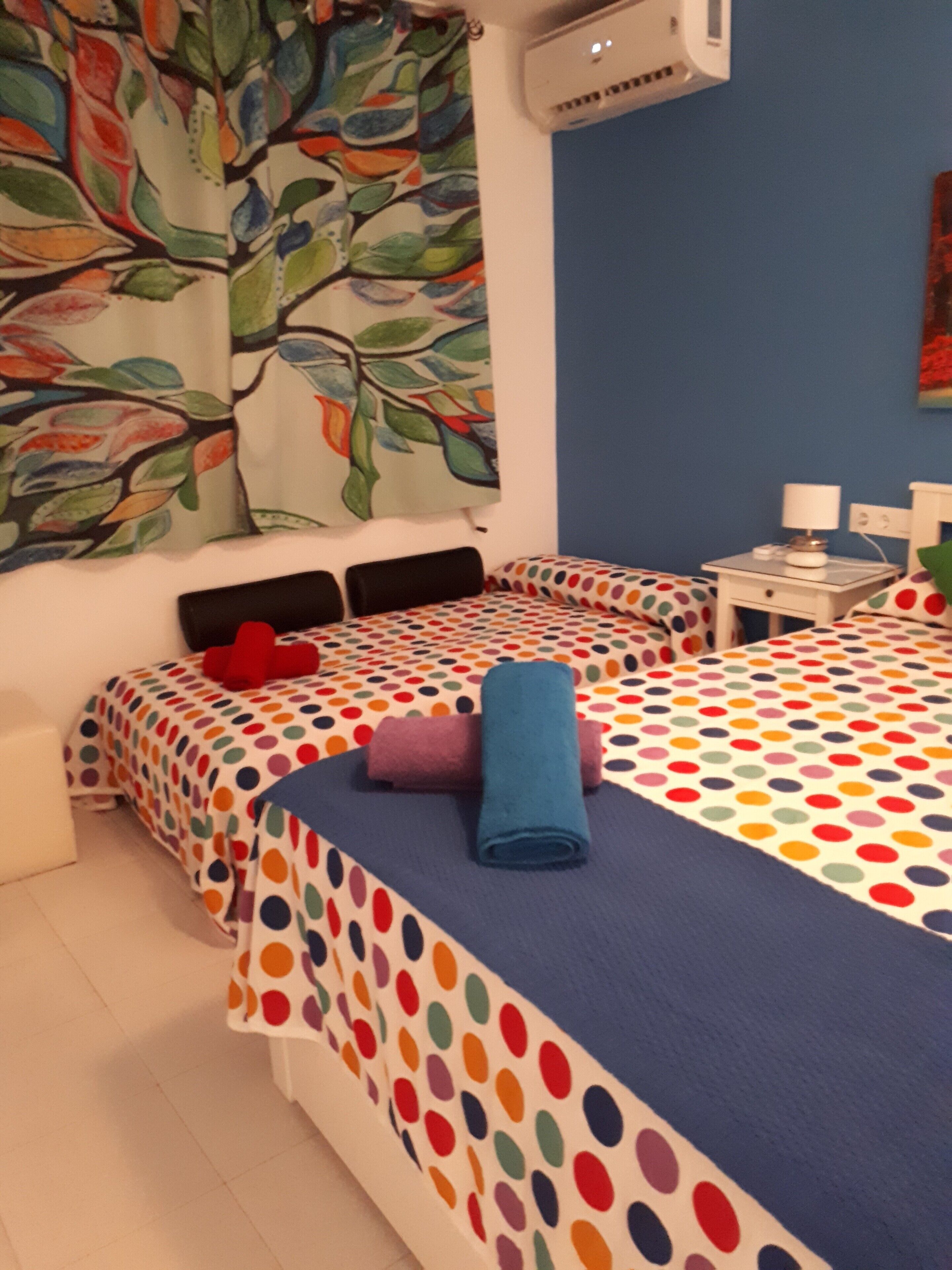A hotel room with two beds, colorful polka dot bedding, a red pillow, and a blue towel.