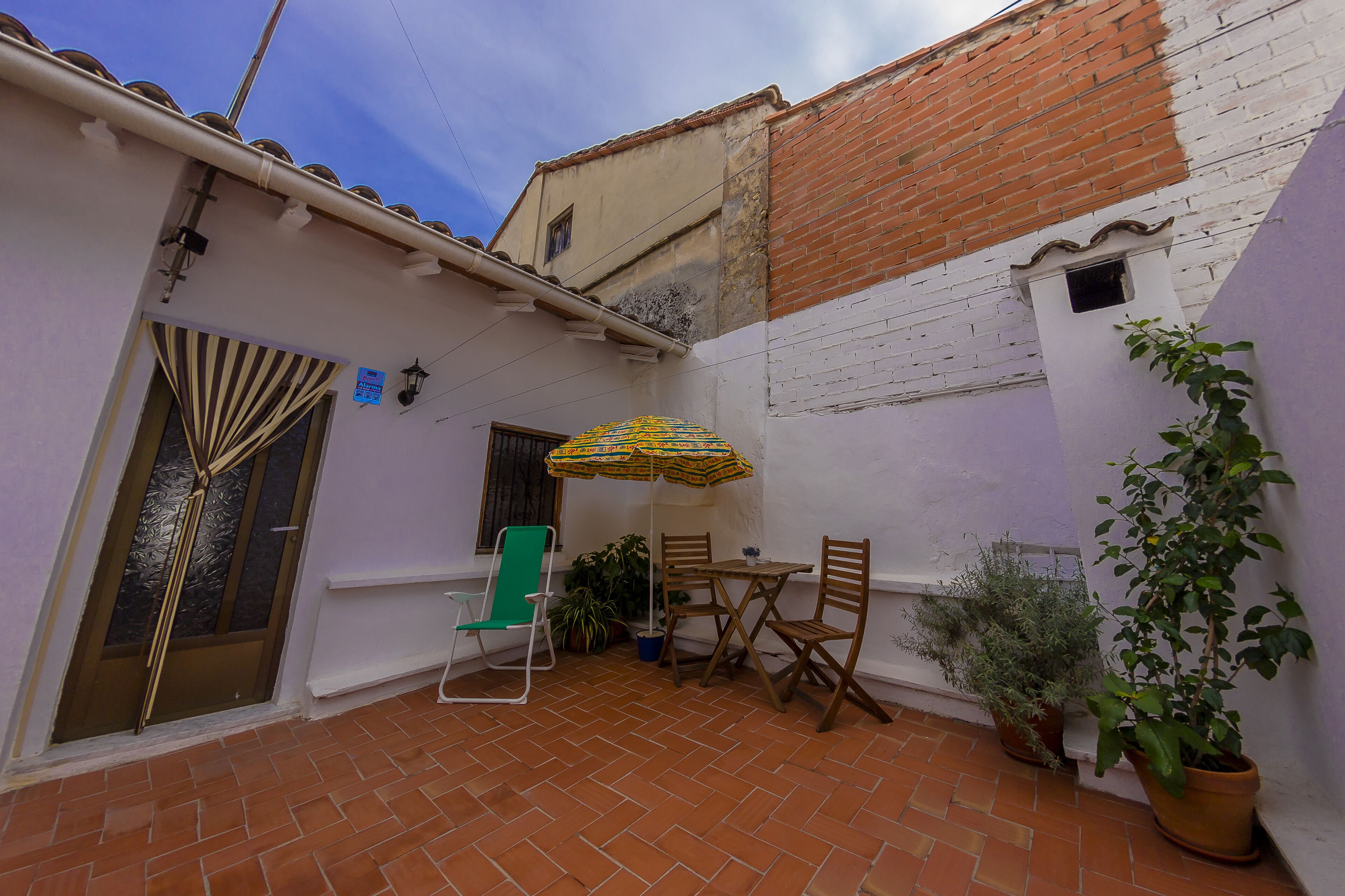 A patio with a table and chairs, a green chair, an umbrella, and potted plants.