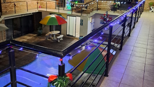 A pool area with a table and chairs, surrounded by a railing with blue lights. There is a Christmas tree and a balcony with a railing. - Hidden Inn (Pietermaritzburg)