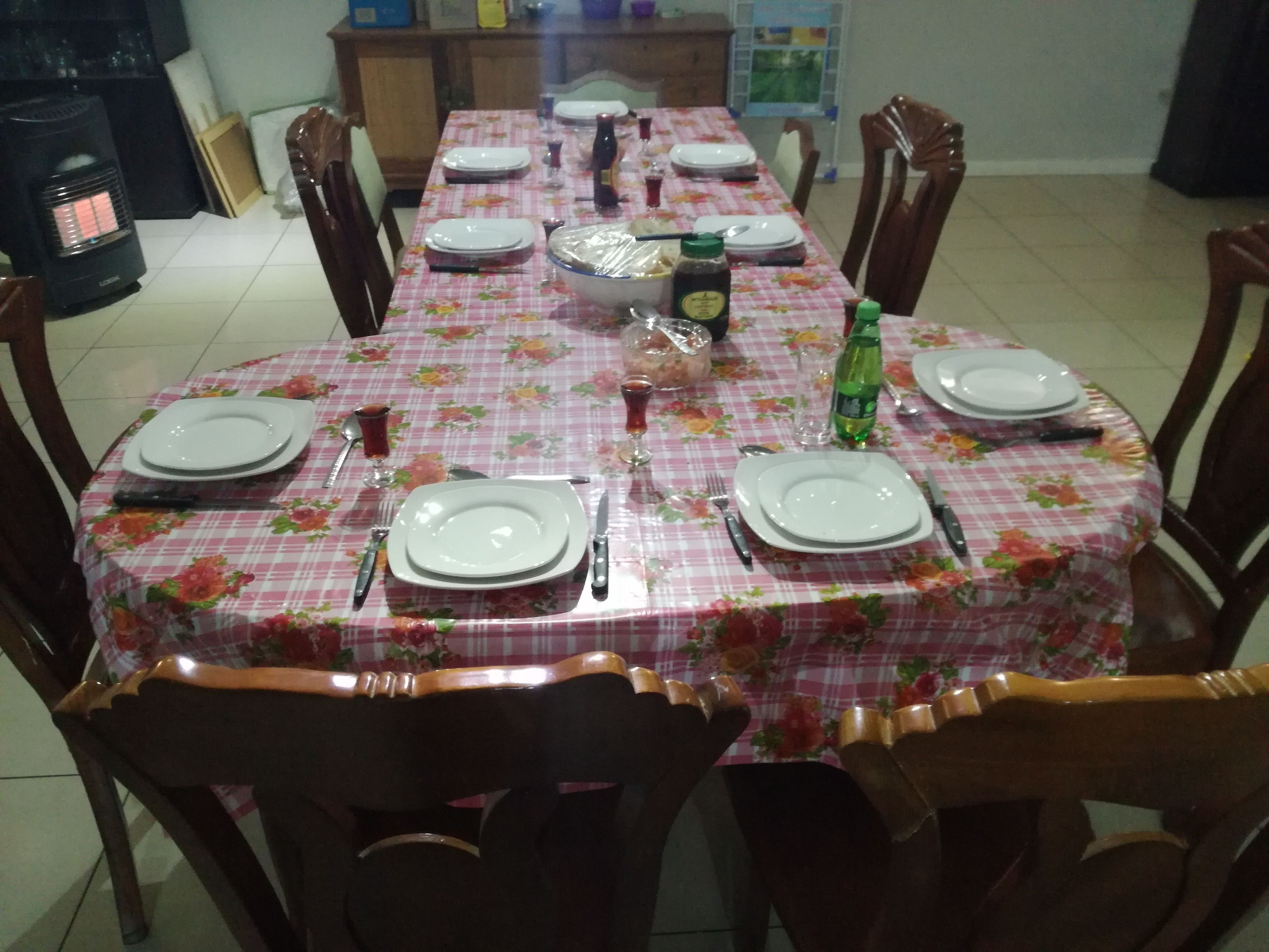 A dining table set with plates, cutlery, and glasses, surrounded by wooden chairs.