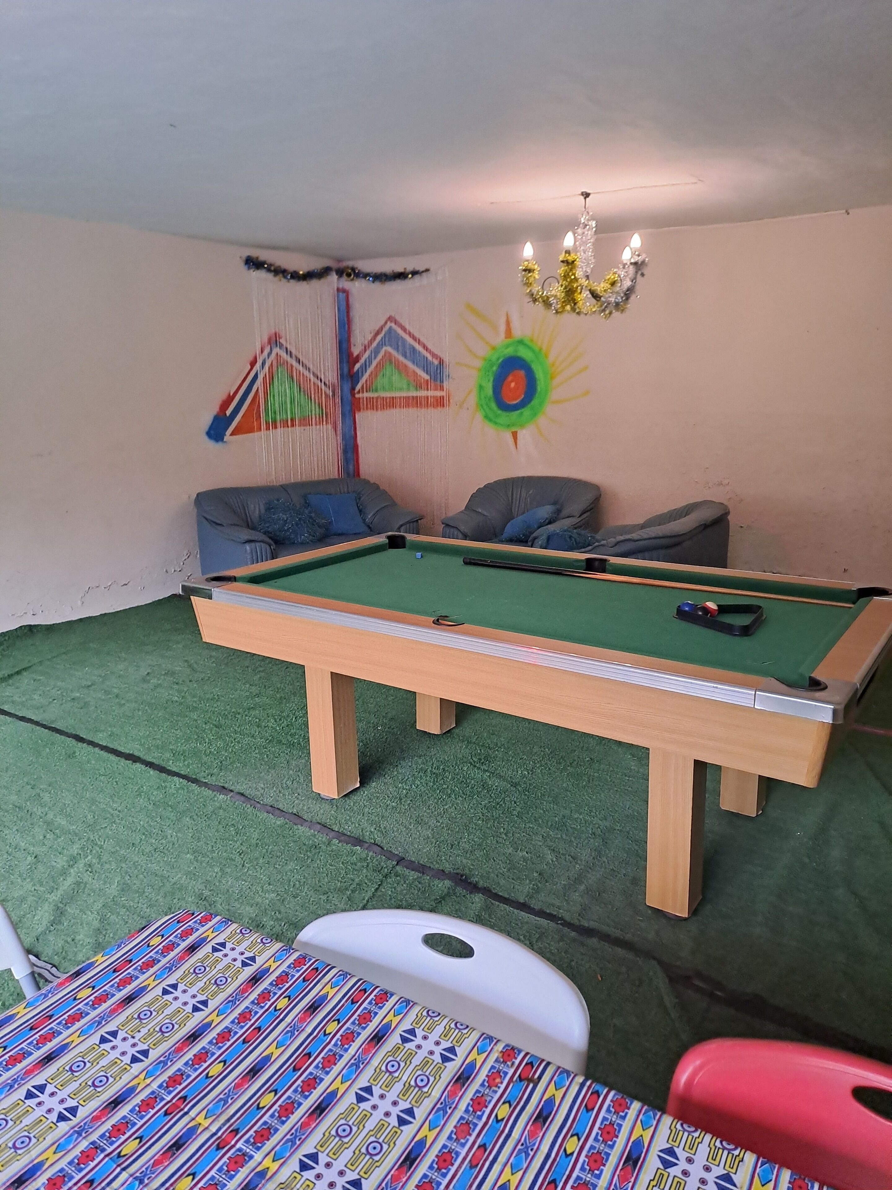 A pool table with a green felt surface, two grey sofas with blue cushions, and a colorful patterned chair.