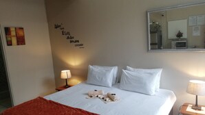 A neatly made bed with white linens and a red blanket, a wall with motivational quotes, a bedside table with a lamp, and a mirror reflecting the room. - Hidden Inn (Pietermaritzburg)