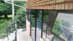 A balcony with a brick wall, glass railings, and a view of greenery. - Hidden Inn (Pietermaritzburg)