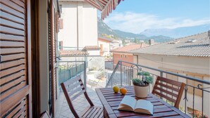 A balcony with a wooden table, two chairs, a potted plant, and an open book. - Casa del Borgo Vesio (Tremosine)