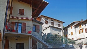 A multi-story building with a balcony, a red garage door, and a staircase leading to the upper floor. - Casa del Borgo Vesio (Tremosine)