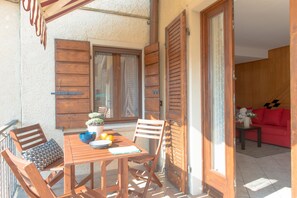Une table en bois placée à l’extérieur, avec des chaises, une plante en pot et un saladier rempli de fruits.