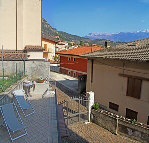 A courtyard with a grill, lounge chairs, and a view of a mountain range. - Casa del Borgo Vesio (Tremosine)