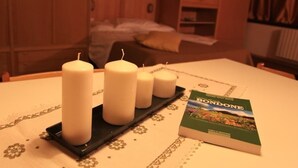 A room with a bed, a bedside table with candles, and a book titled "BONDONE". - Residence Prada (Trento)