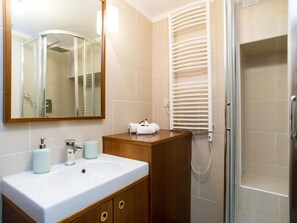 A bathroom with a white sink, wooden vanity, a glass shower enclosure, and a towel rack.