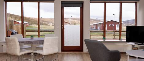 Una sala de estar moderna con un ventanal grande, un televisor y una zona de comedor con sillas y una mesa.