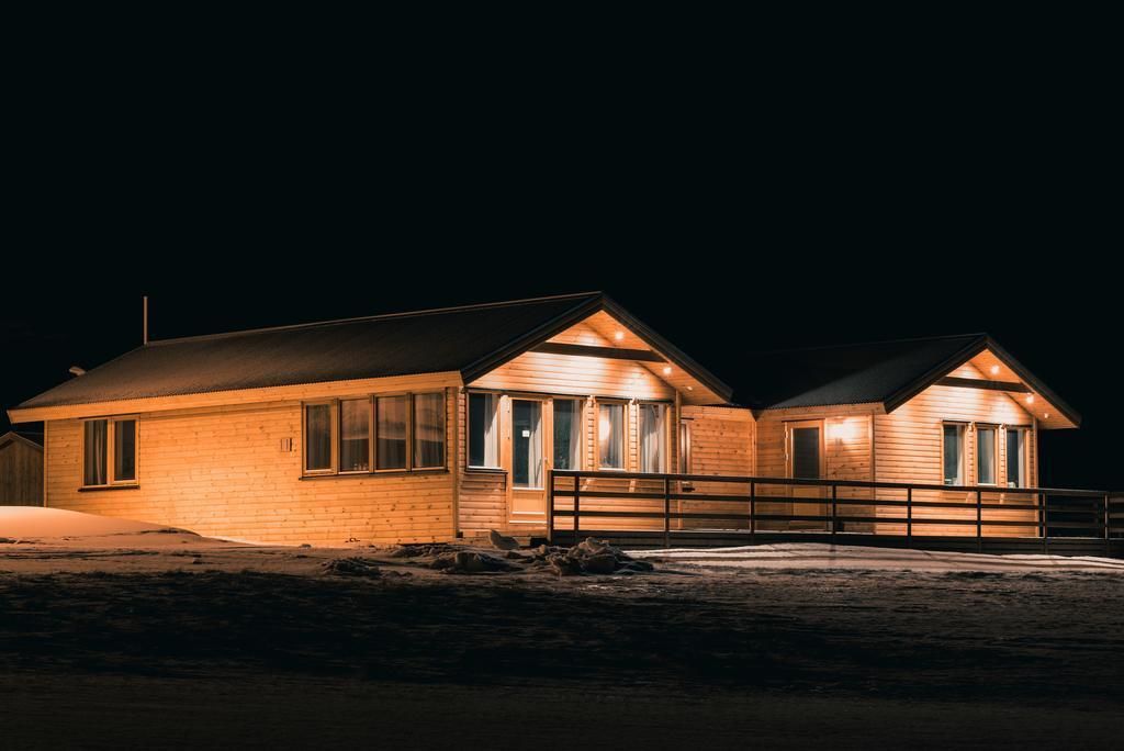 A two-story wooden cabin with a balcony, illuminated by warm interior lighting.