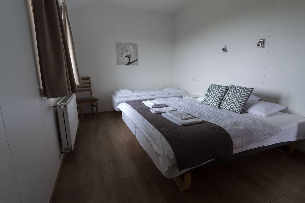 A room with two single beds, a chair, a radiator, and a wall-mounted artwork.