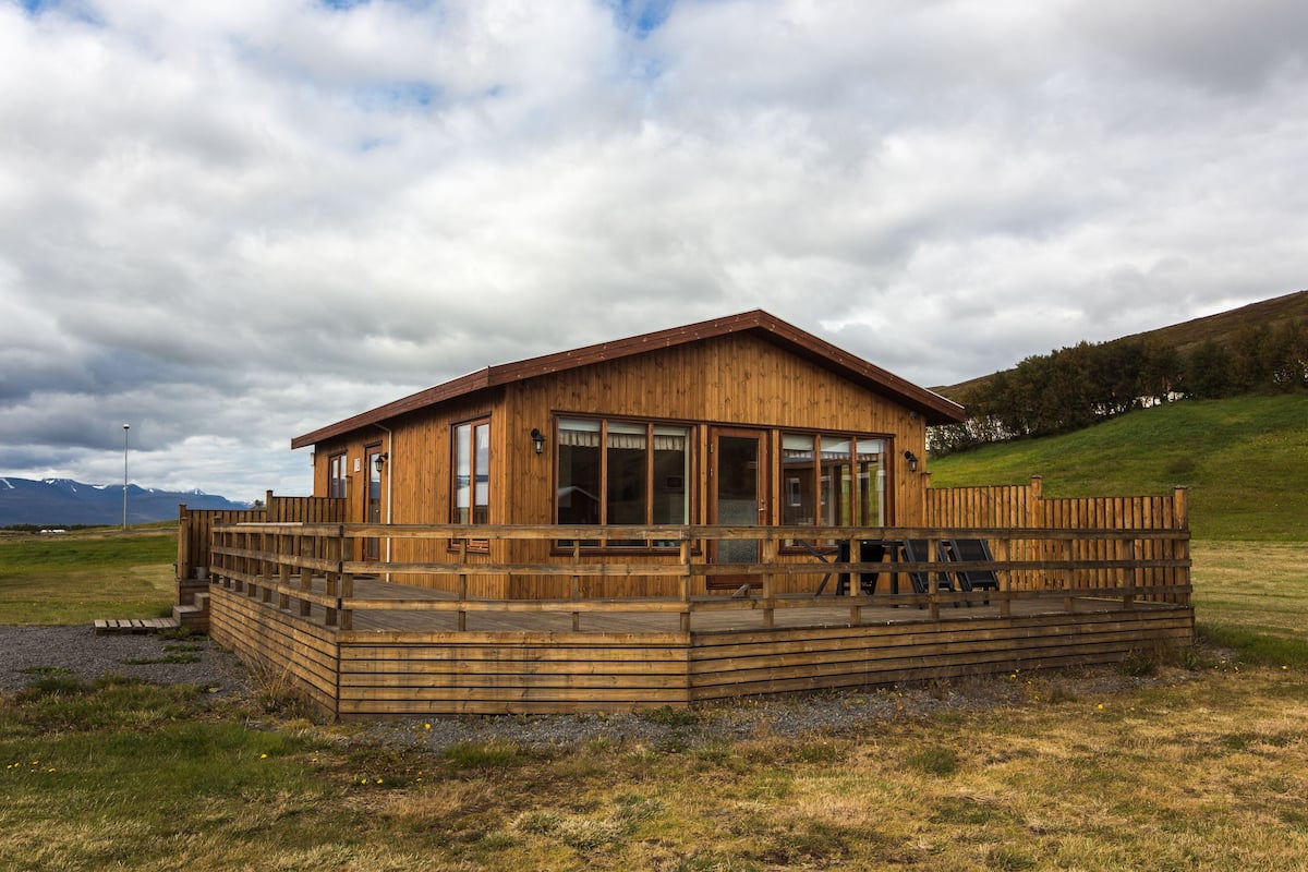 A wooden cabin with a deck, large windows, and a view of the surrounding landscape.
