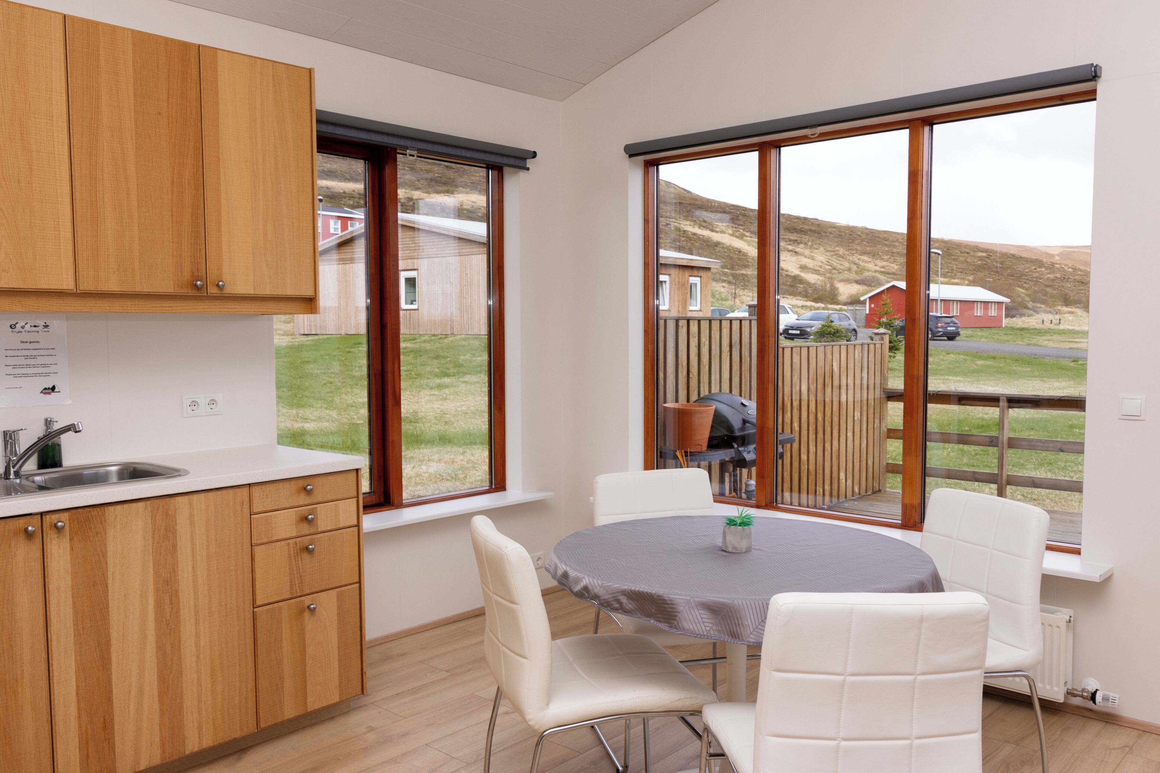 A modern kitchen with wooden cabinets, a white countertop, and a large window offering a view of a rural landscape.