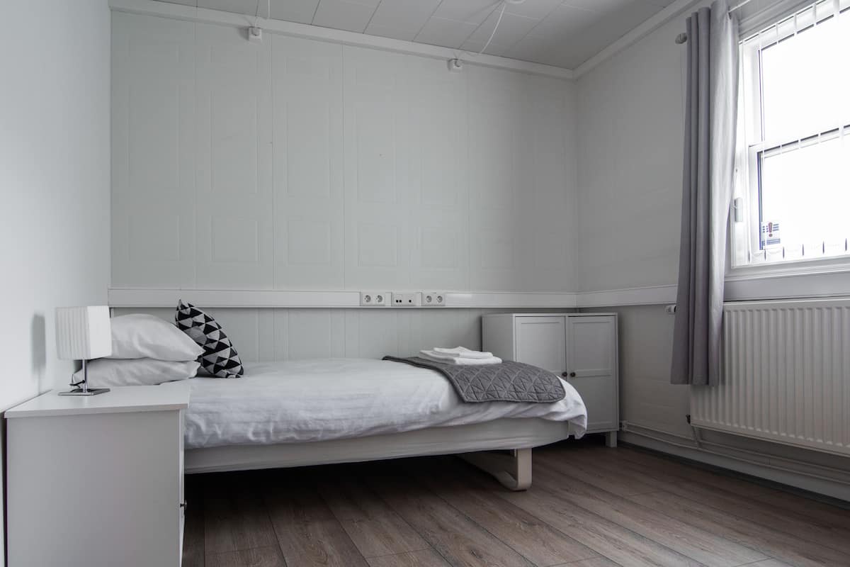 A bedroom with a single bed, a bedside table, a lamp, and a window with curtains.