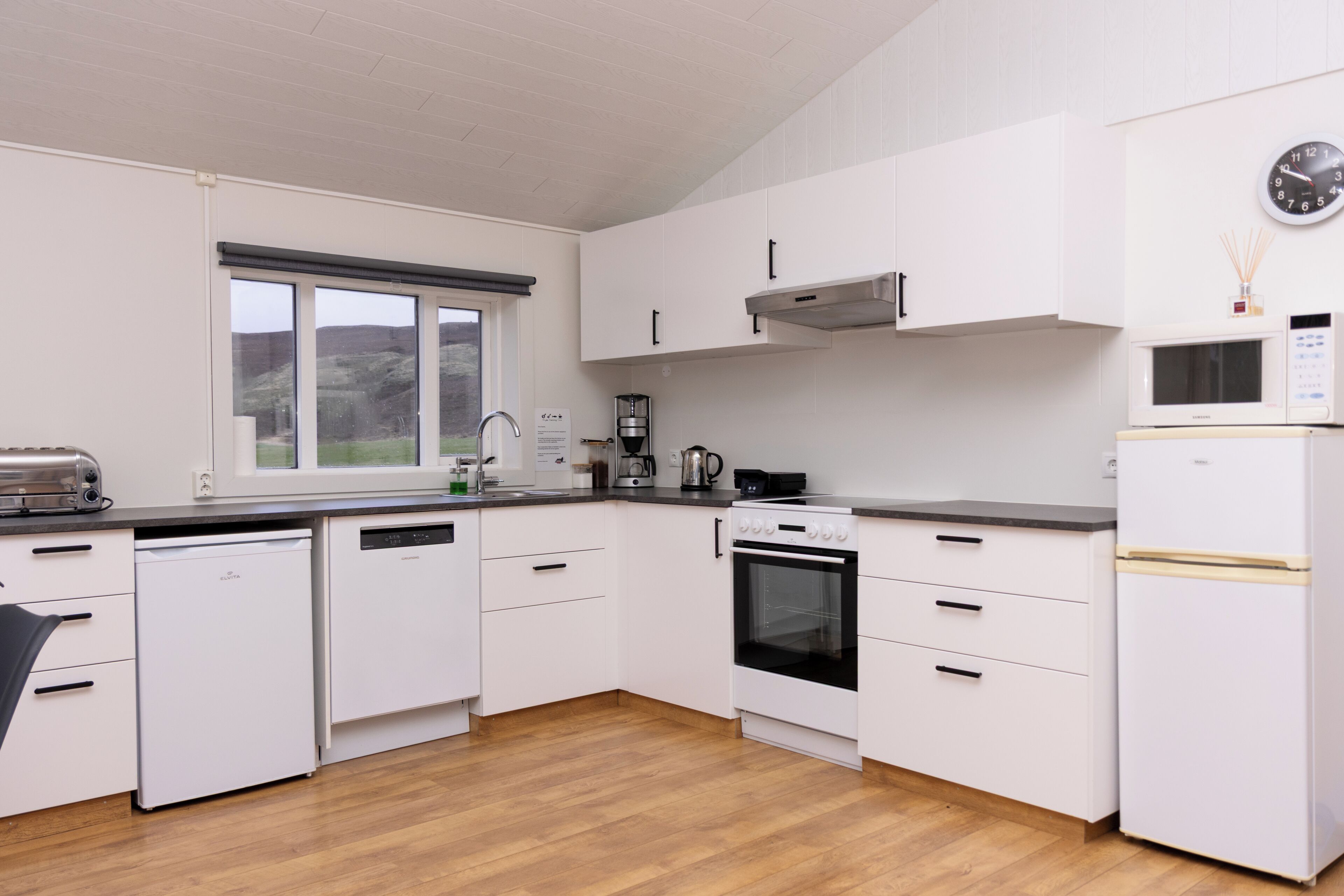 Una cocina moderna con armarios blancos, lavavajillas, horno, microondas y refrigerador.
