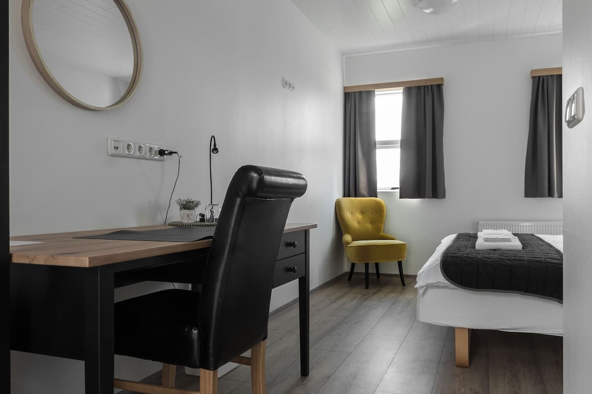 A modern room with a wooden desk, a black chair, a yellow armchair, a bed, and a window with curtains.