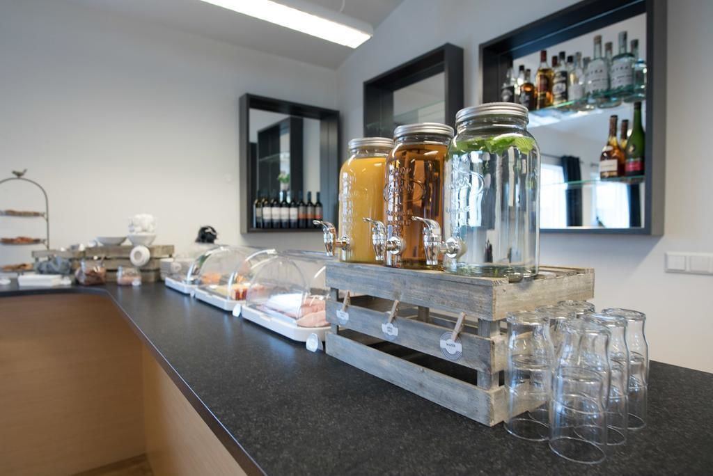 A bar area with a wooden counter, glass jars with drinks, and a wine shelf in the background.