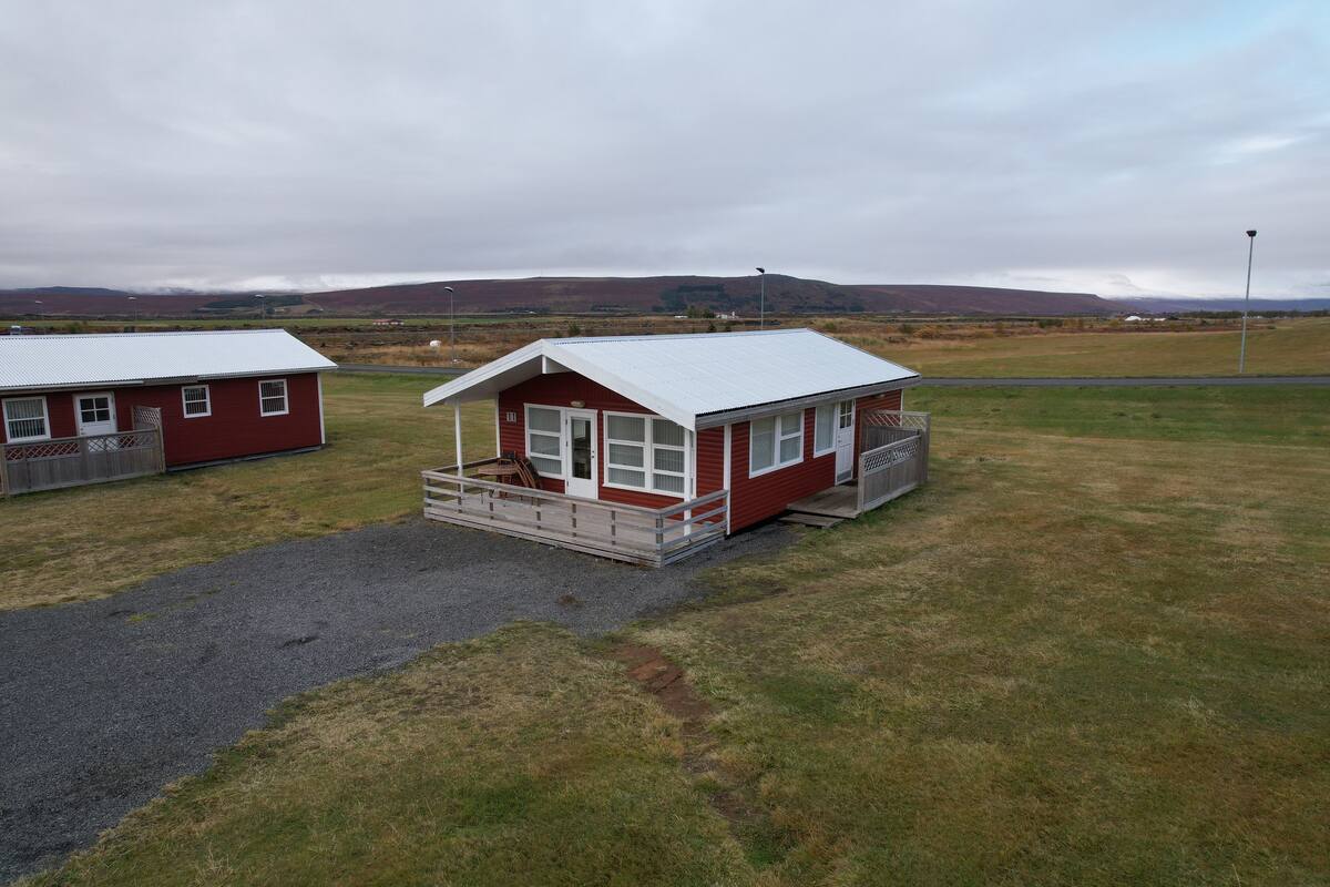Two red buildings with white roofs, a gravel path, and a grassy field.