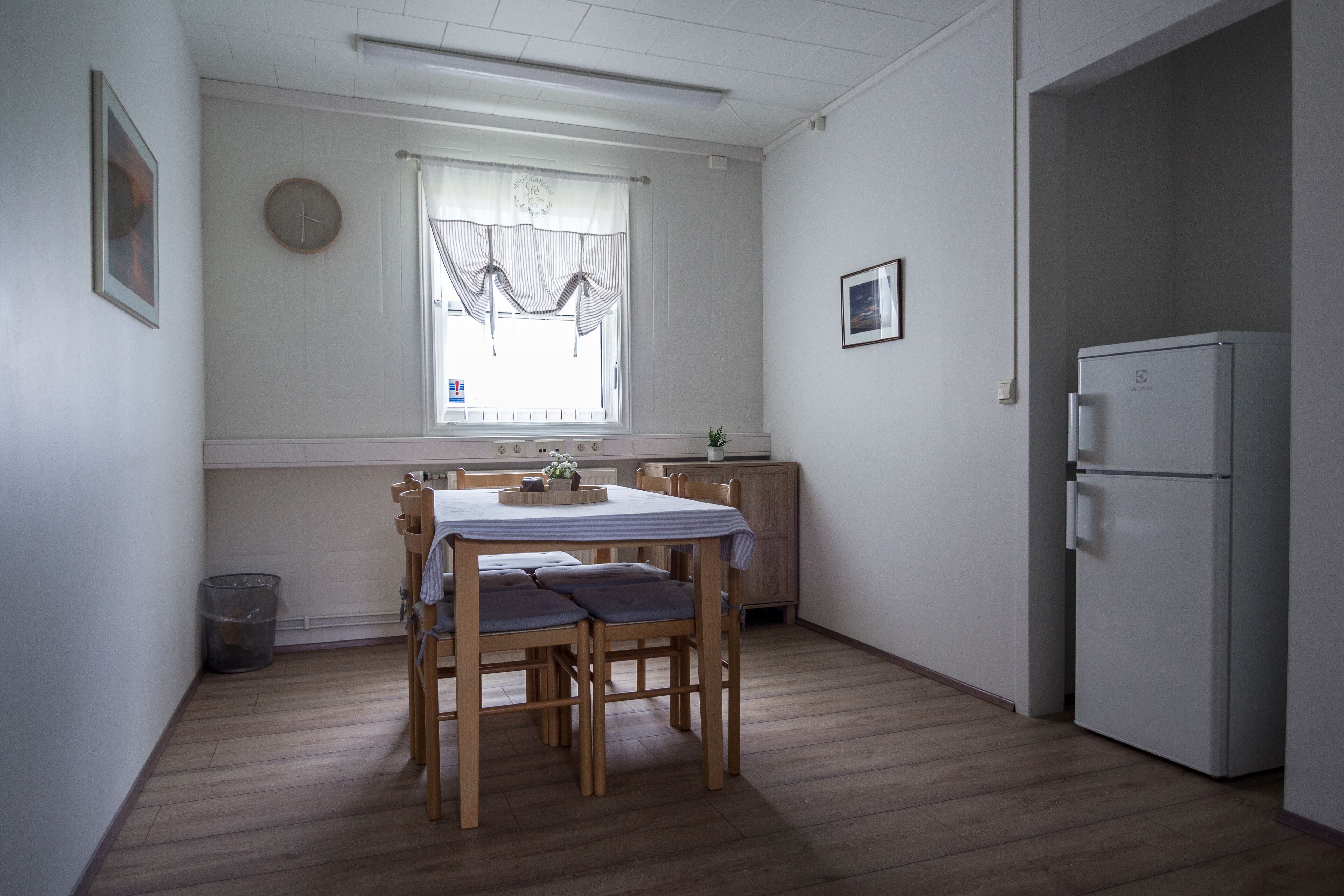 Kompakti keittiö, jossa on ruokapöytä, tuolit, jääkaappi ja ikkuna, jossa on verhot.