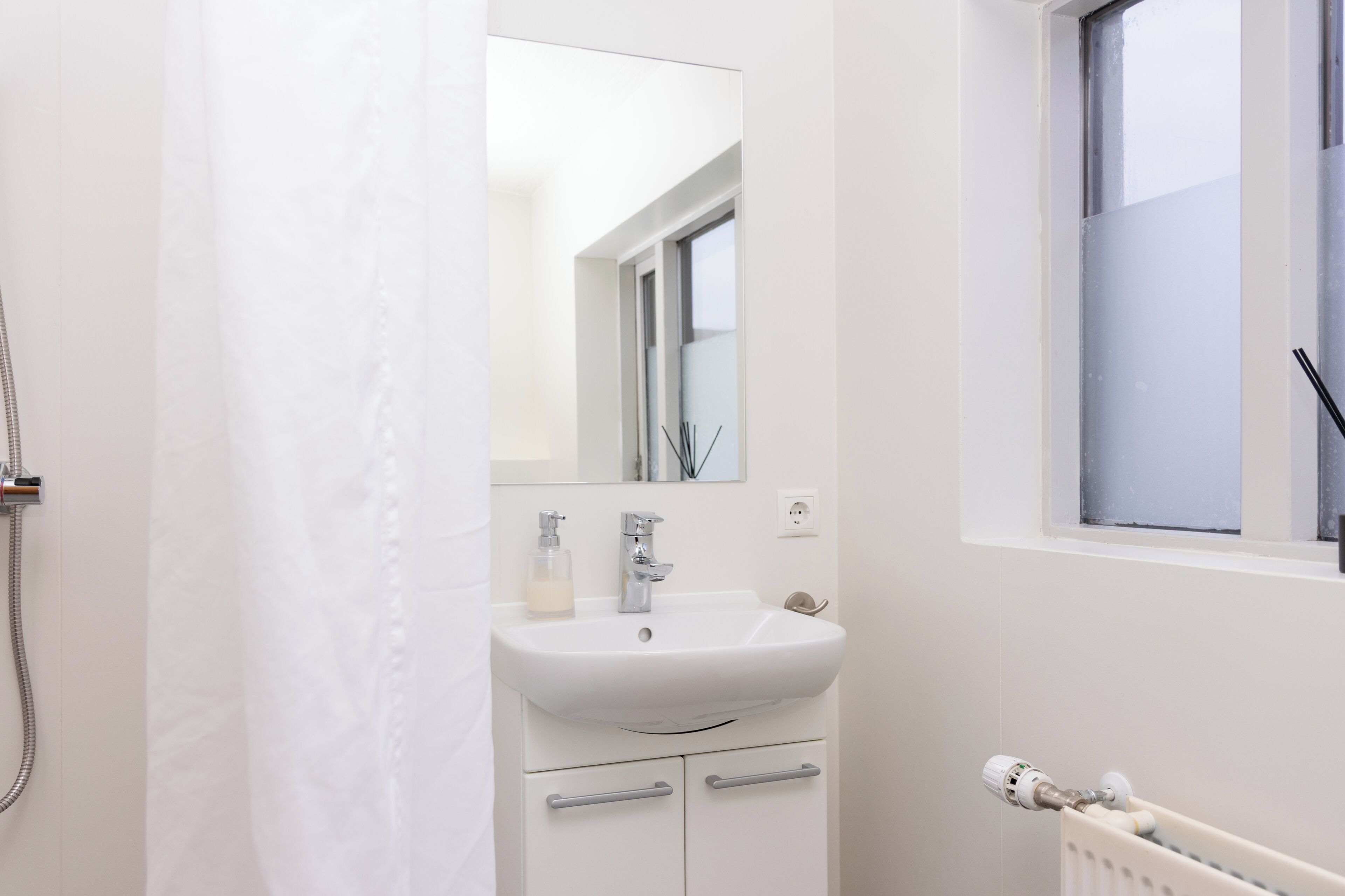 Un baño con lavamanos blanco, espejo y ventana.