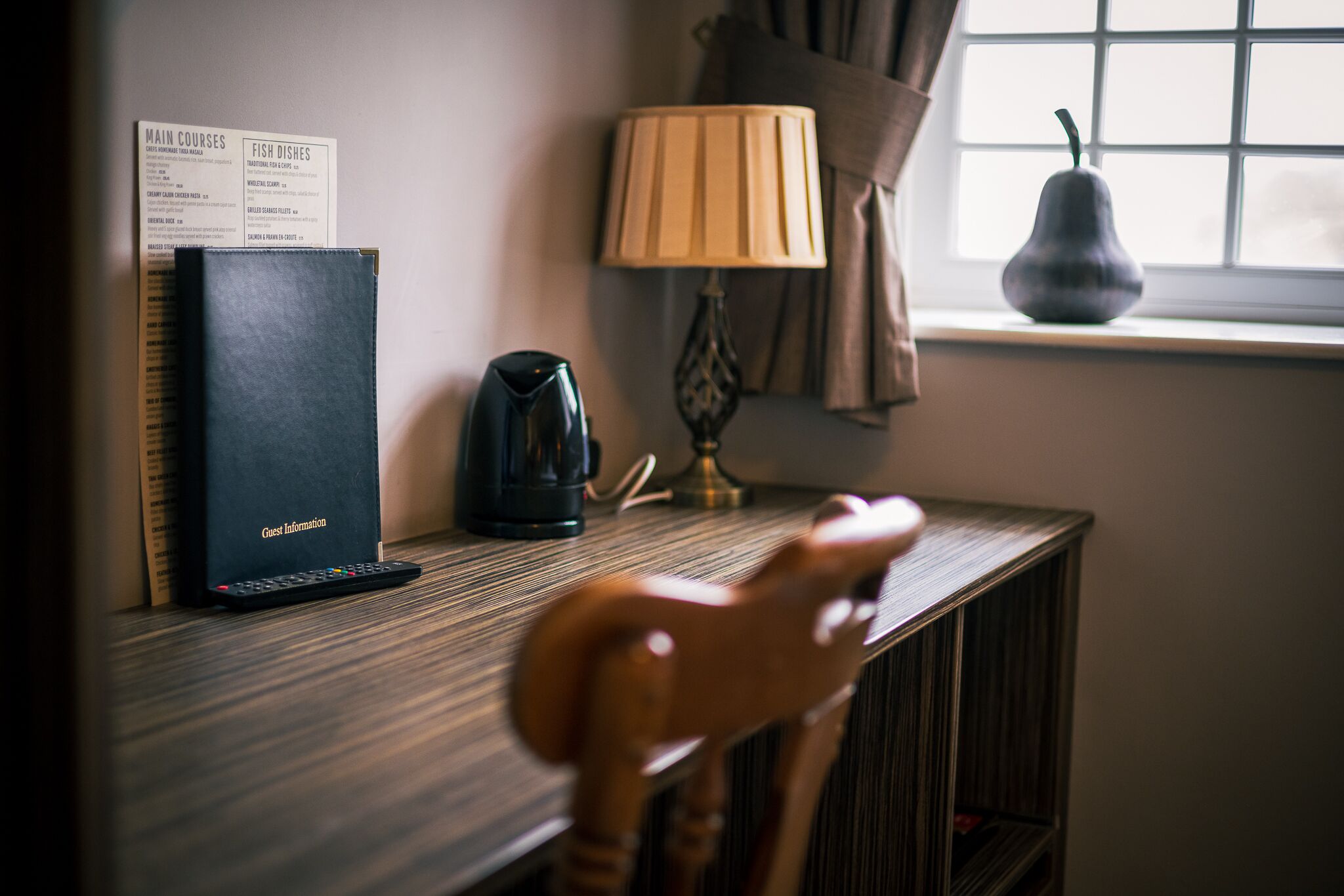 A wooden chair with a curved backrest, a black electronic device labeled 'Guest Information', a lamp, and a vase on a window sill.