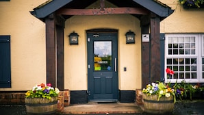 A building entrance with a dark door labeled "HORSE SHOE" and two flower pots on either side.