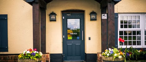 A building entrance with a dark door labeled "HORSE SHOE" and two flower pots on either side.