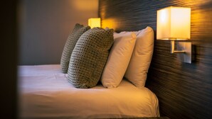 A neatly made bed with a textured pillow and a wall-mounted lamp.