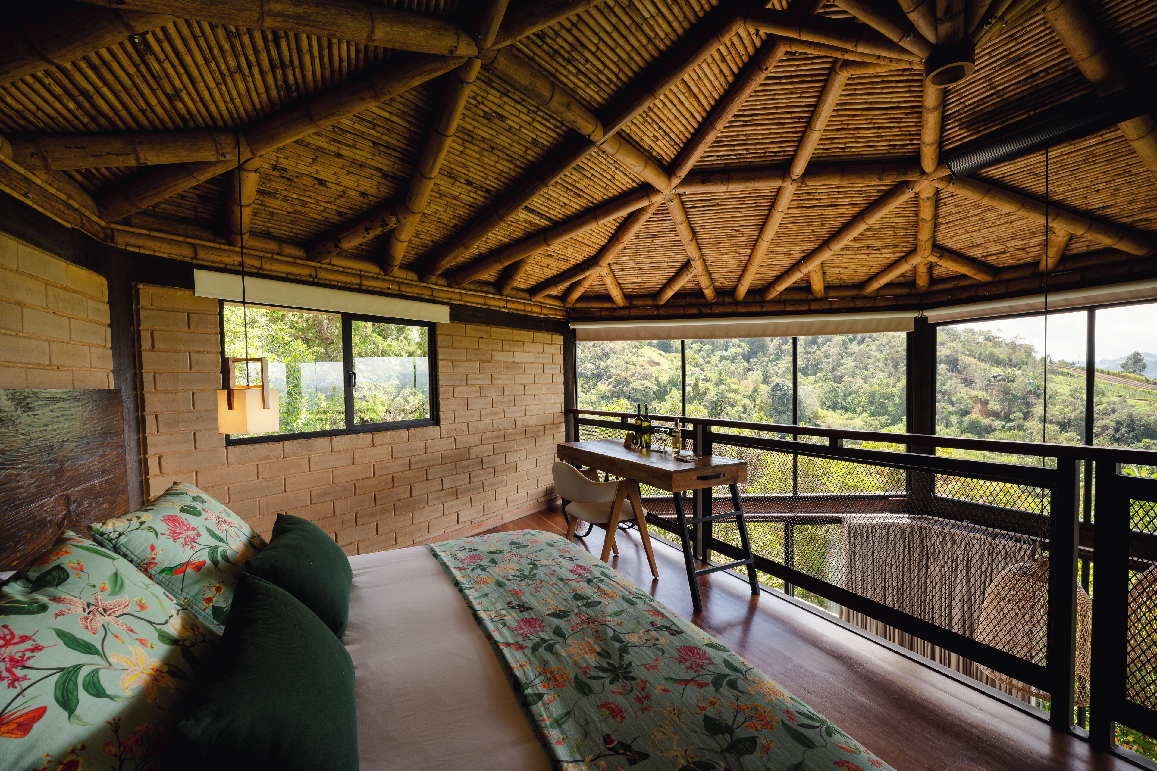 A room with a bed, a desk, and a balcony with a view of the countryside.