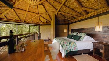 A room with a wooden ceiling, a bed with floral bedding, a wooden table with glasses and a bottle, and a view through large windows.