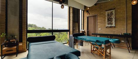 A room with massage tables, a view of greenery, and a brick wall.