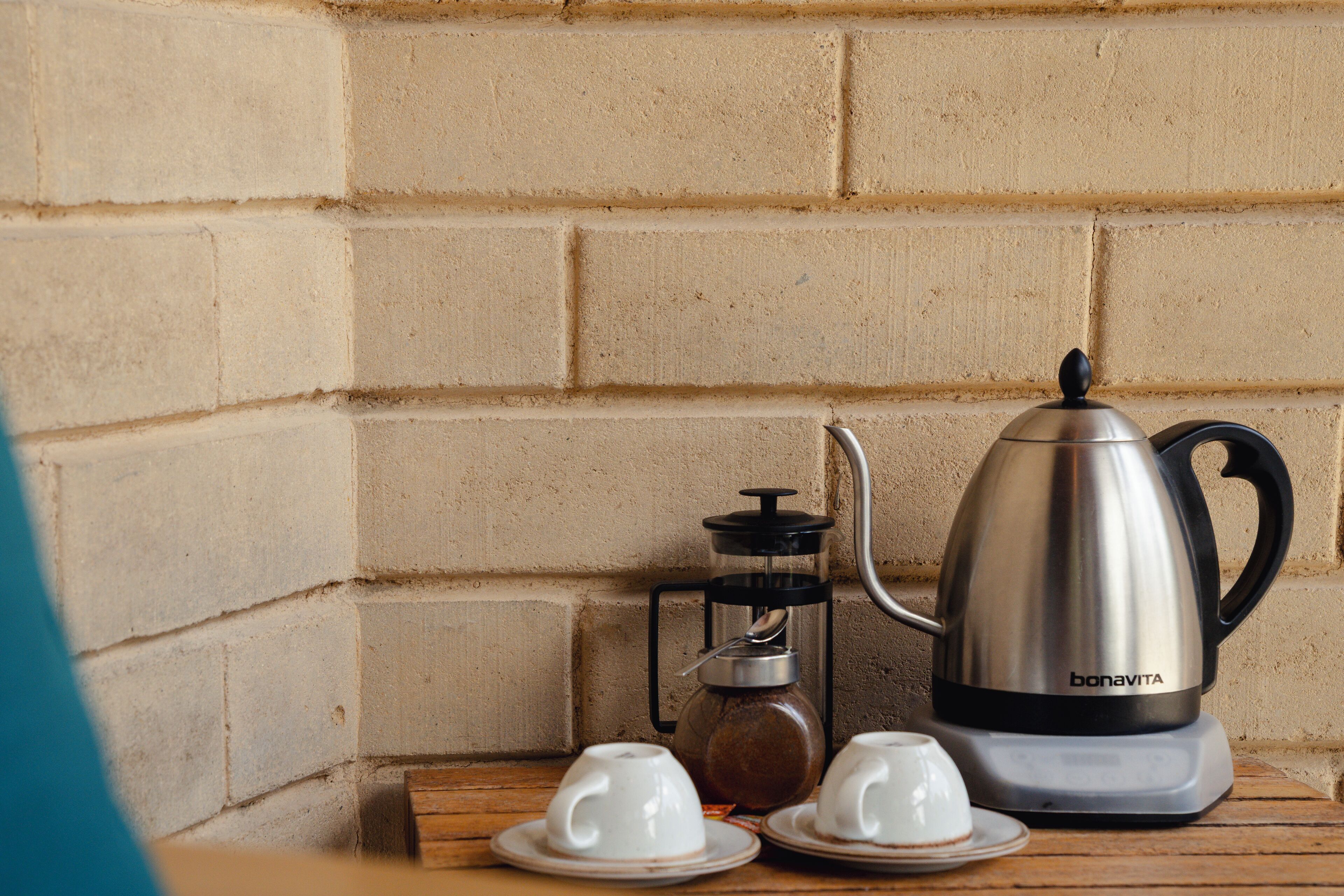 A coffee maker, two white cups, and a glass carafe on a wooden table against a brick wall.