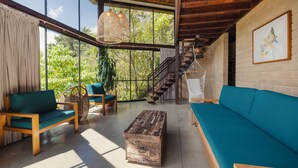 Un amplio espacio habitable con una escalera de madera, un ventanal con cortinas y un sofá color turquesa.
